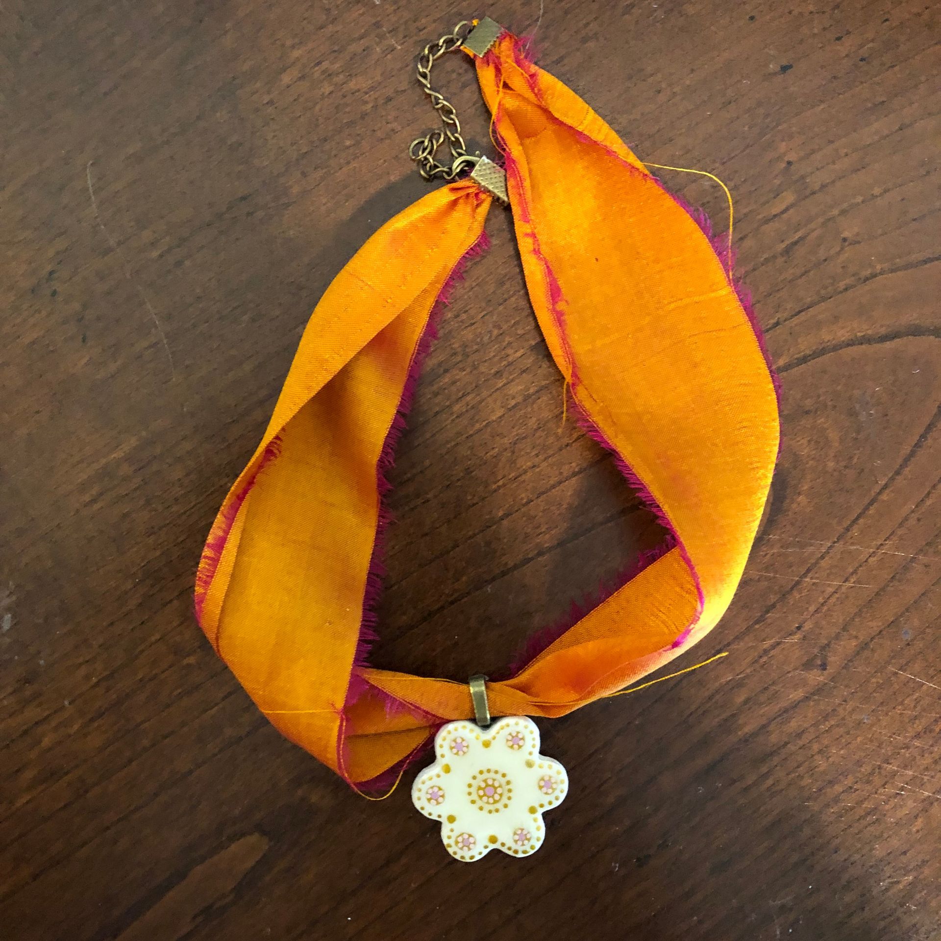 Orange ribbon necklace with a white flower pendant on a wooden surface.