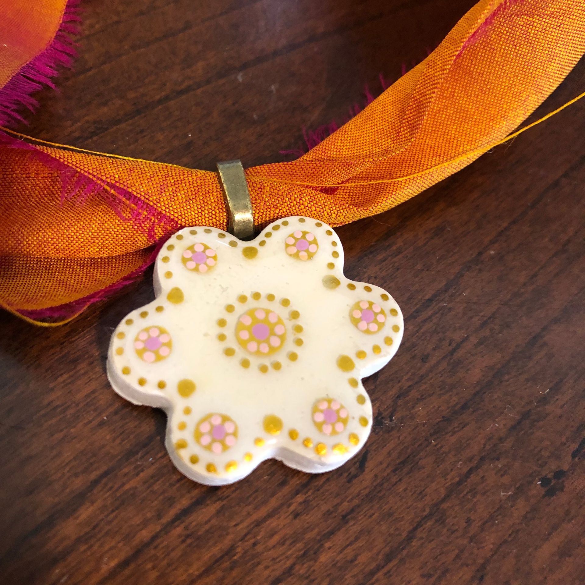 Orange ribbon necklace with a white flower pendant on a wooden surface.