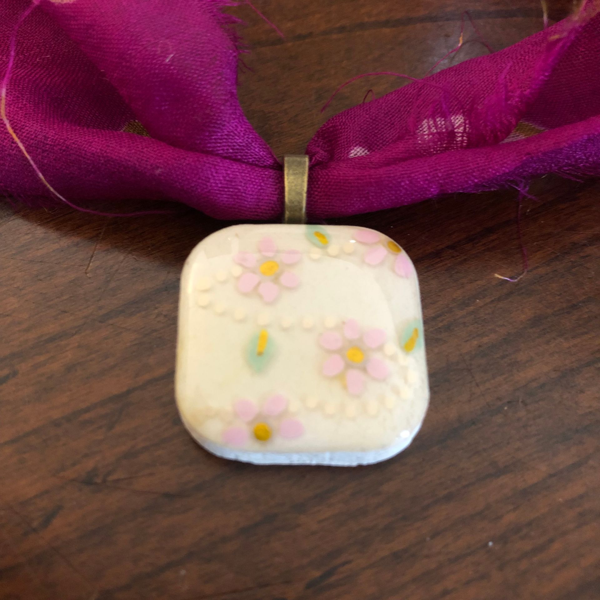 Purple scarf necklace with a white square pendant, gold chain, and wooden background.