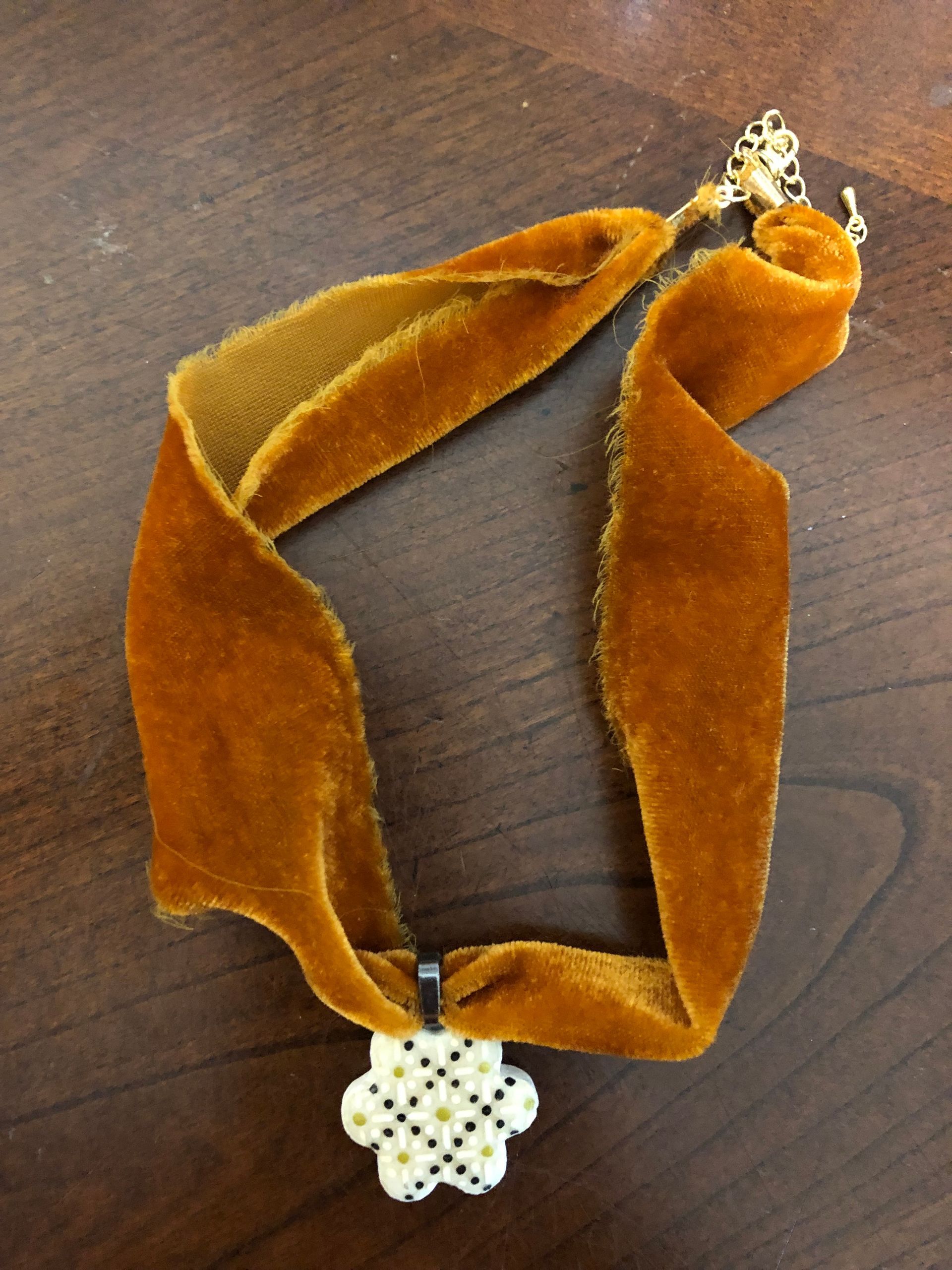 Gold velvet choker necklace with white and yellow flower pendant.