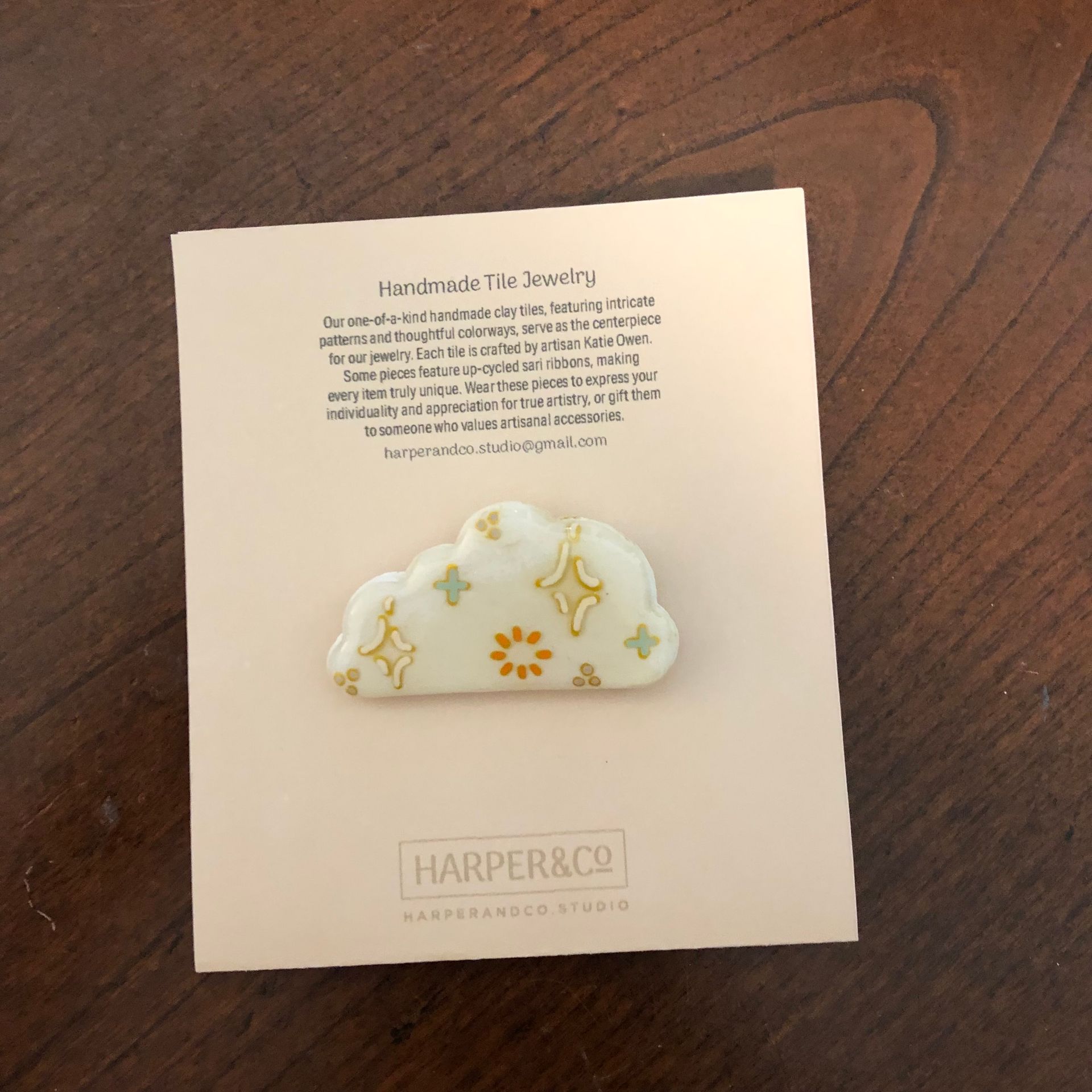 Cloud-shaped pin on a pink card. Pin is white with yellow and green star and sunburst designs.