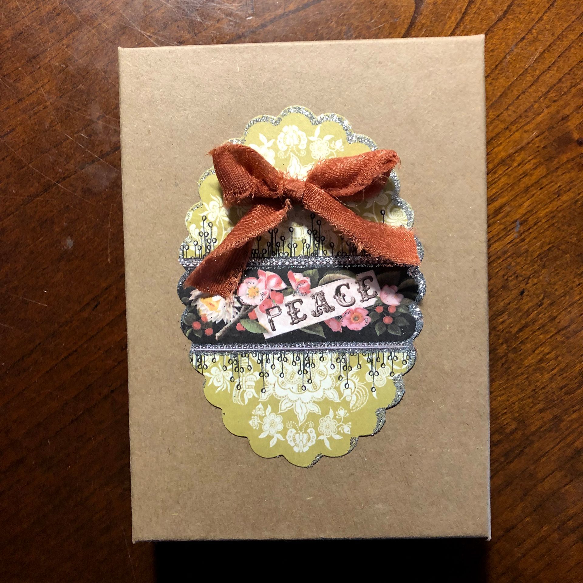 Tan gift box decorated with a layered oval design and an orange ribbon. Text 