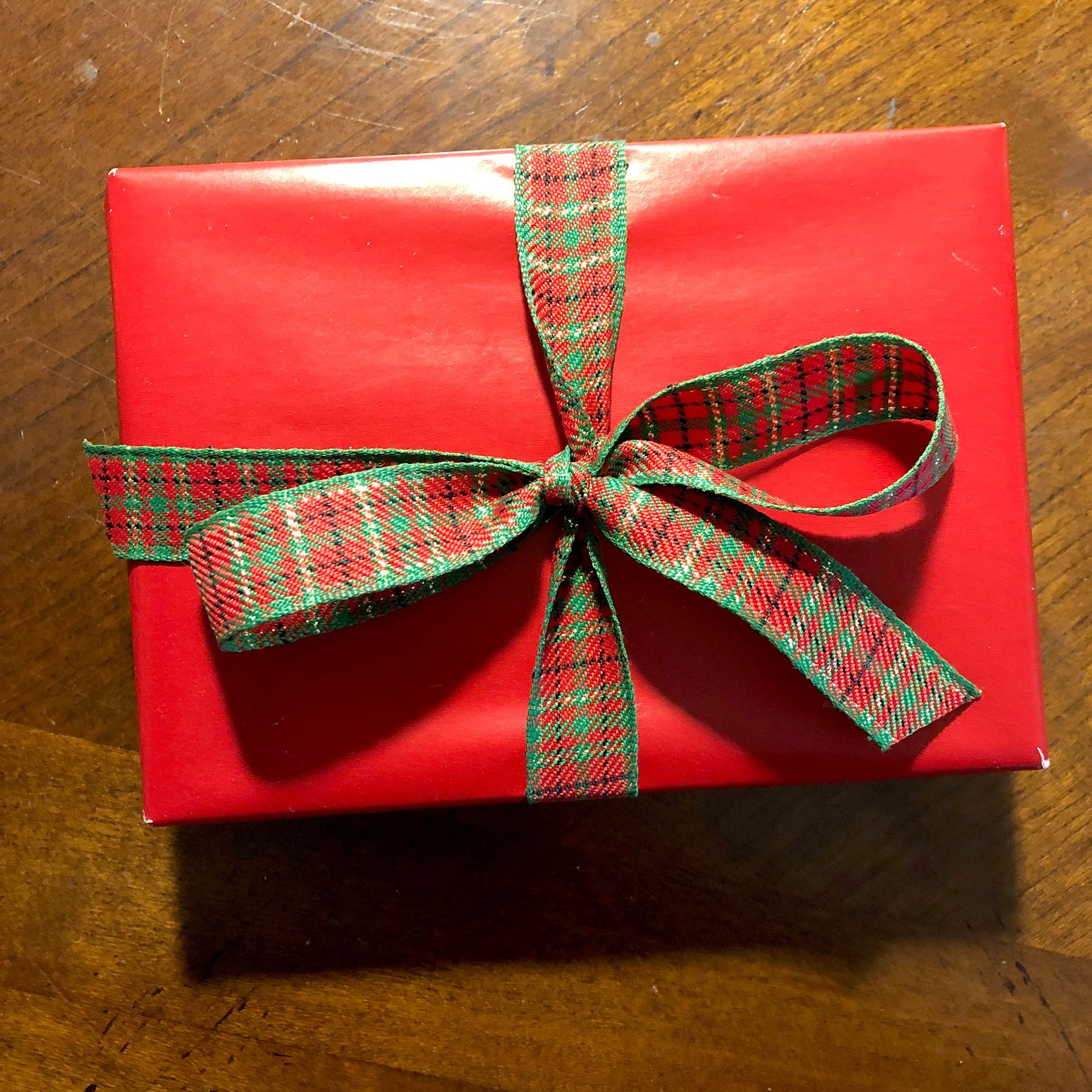 Red wrapped gift with green and red plaid ribbon bow on a wooden surface.