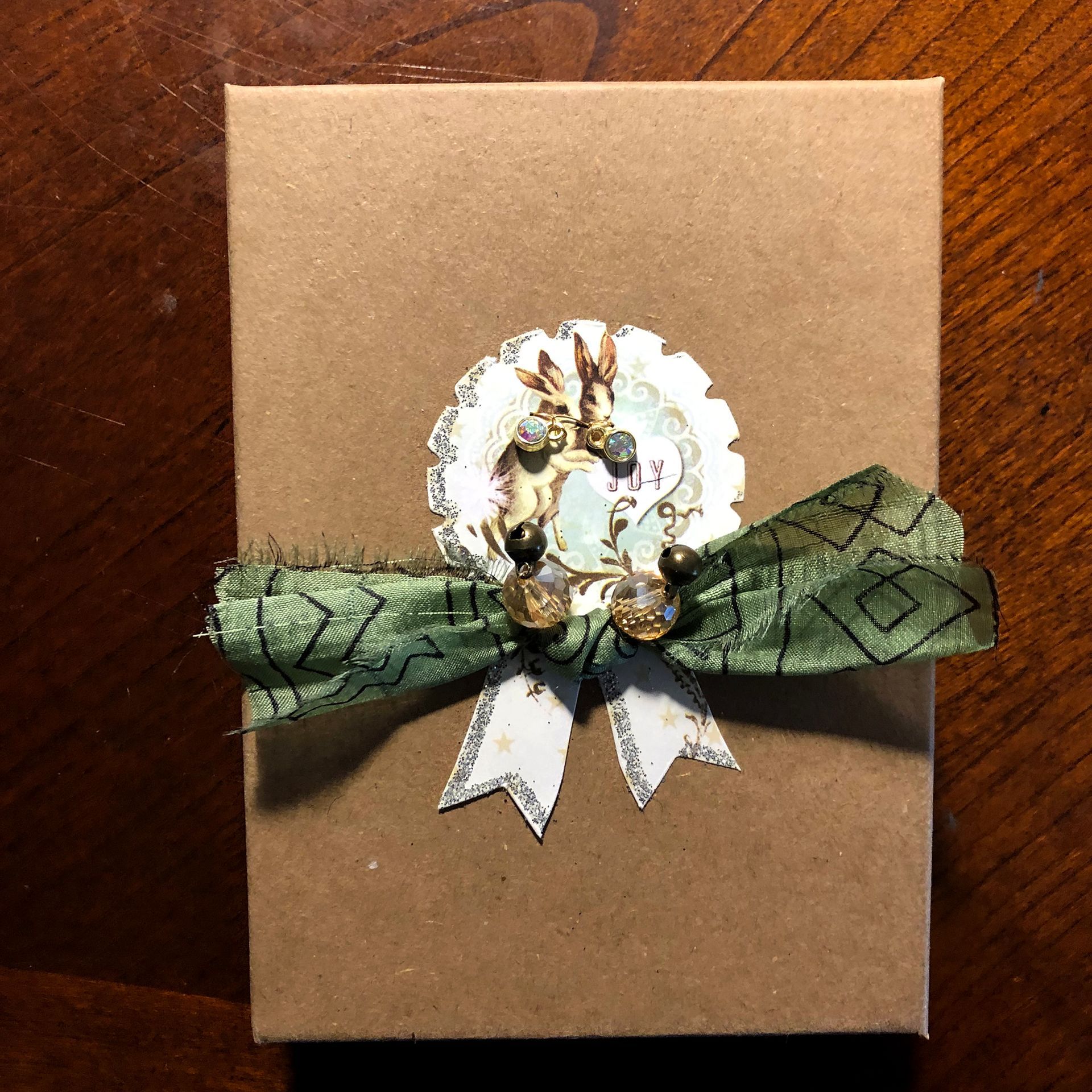Brown gift box with green patterned ribbon, decorated with a floral motif and silver accents.