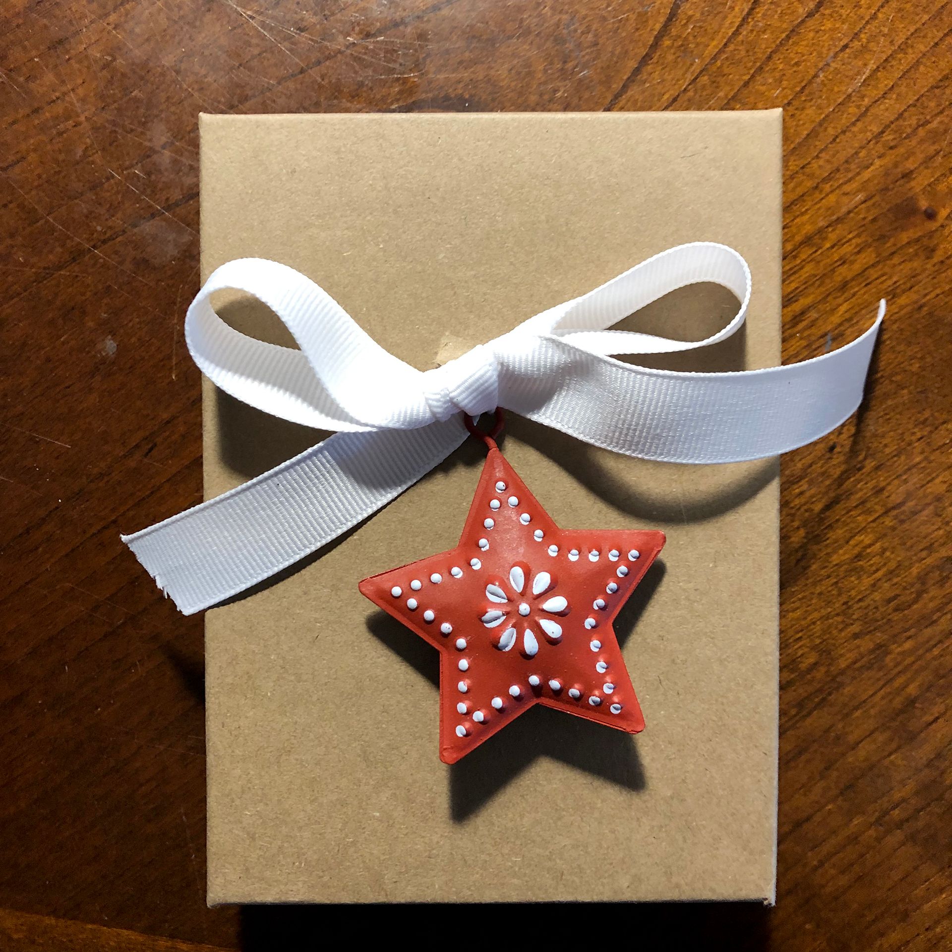 Gift box with white ribbon and a red star ornament.