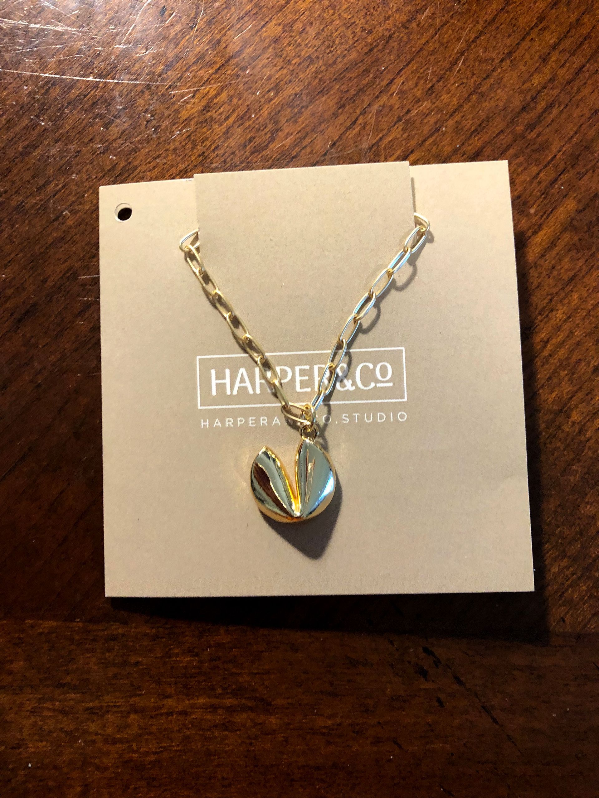 Gold-colored necklace with a fortune cookie pendant on a display card.