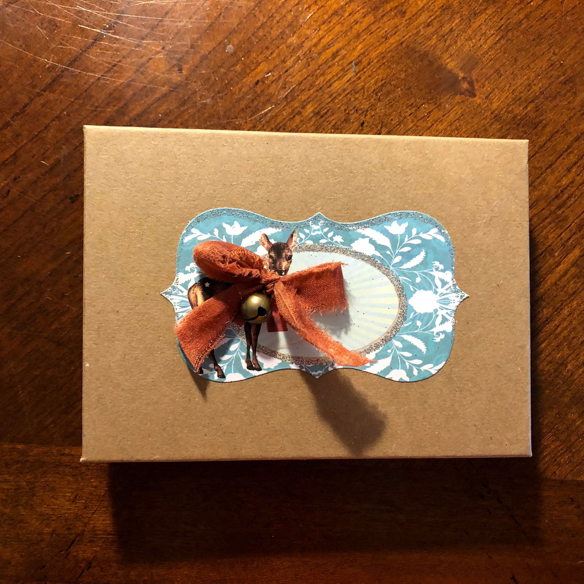 Brown gift box with a decorated label and a small deer figurine.