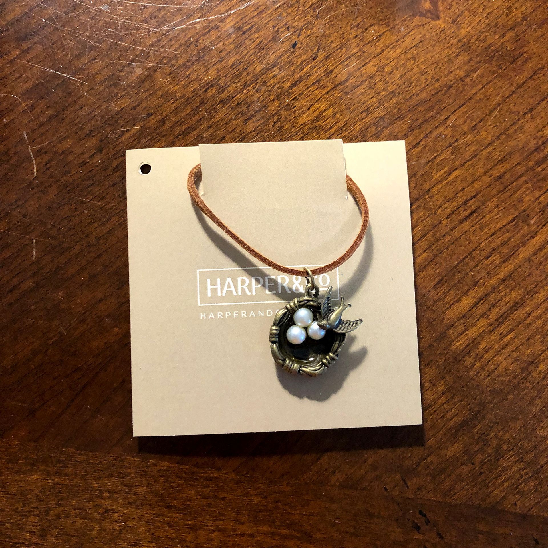 Necklace with bird nest pendant and three pearls on tan tag.