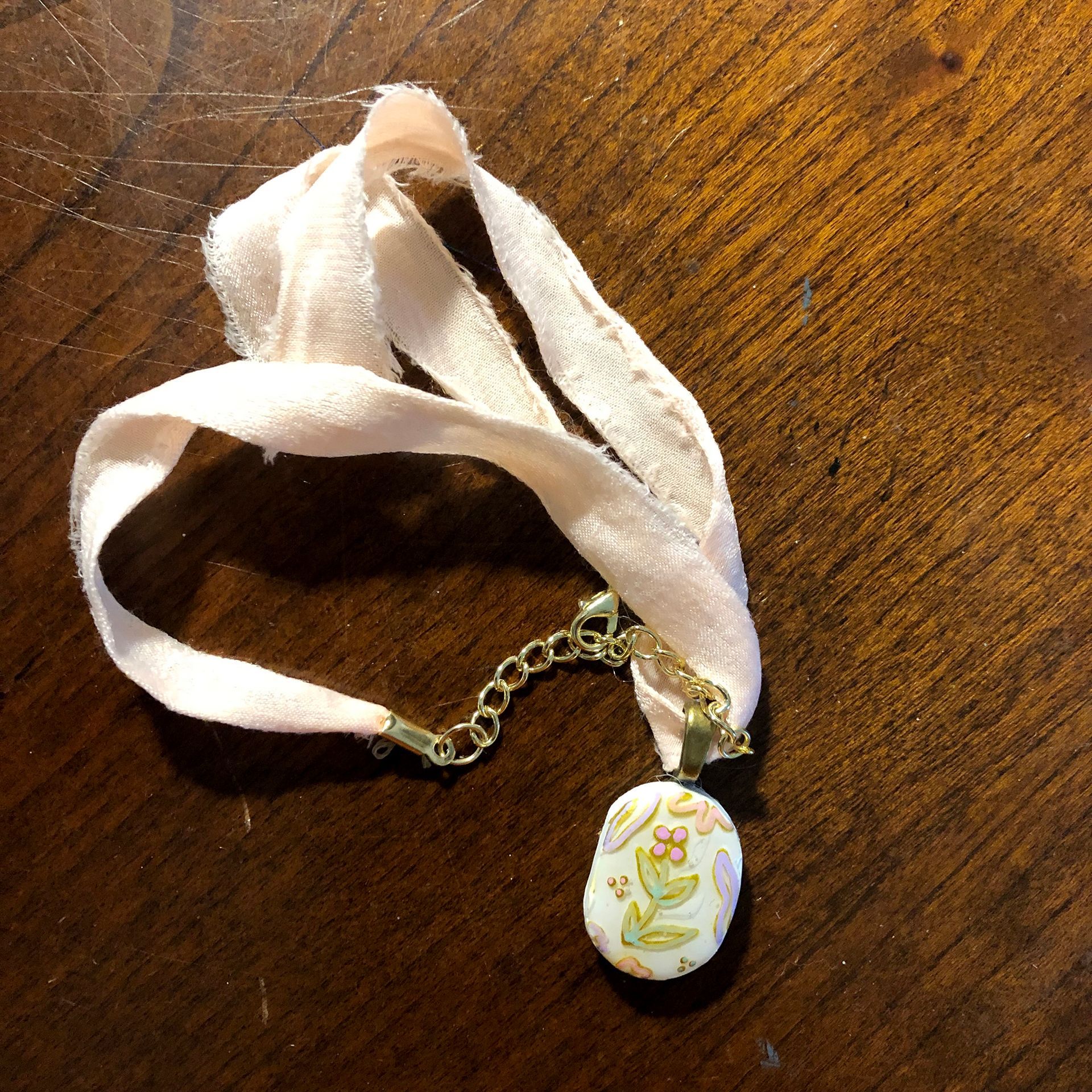 Pale pink ribbon necklace with a floral pendant on a wooden surface.