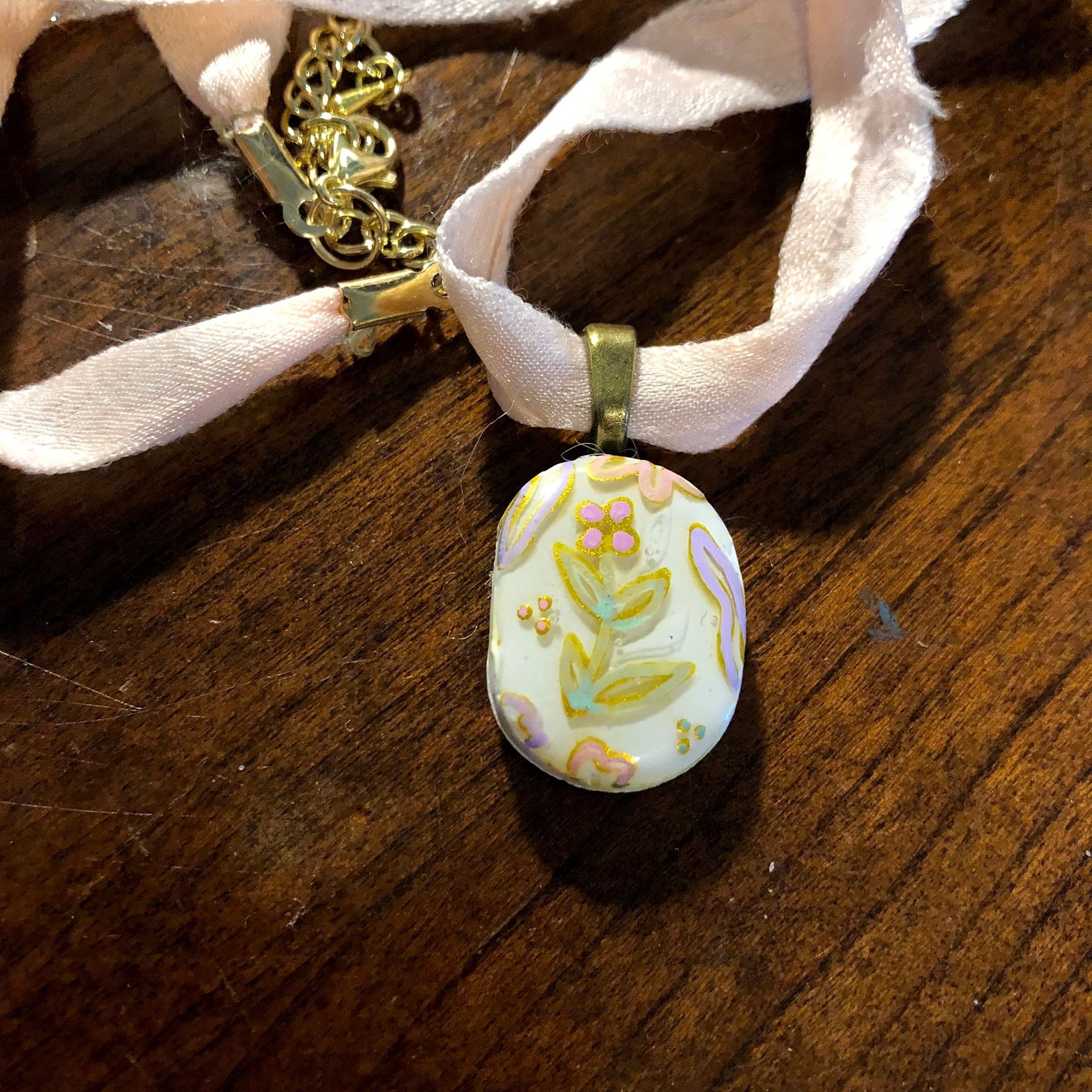 Pale pink ribbon necklace with a floral pendant on a wooden surface.
