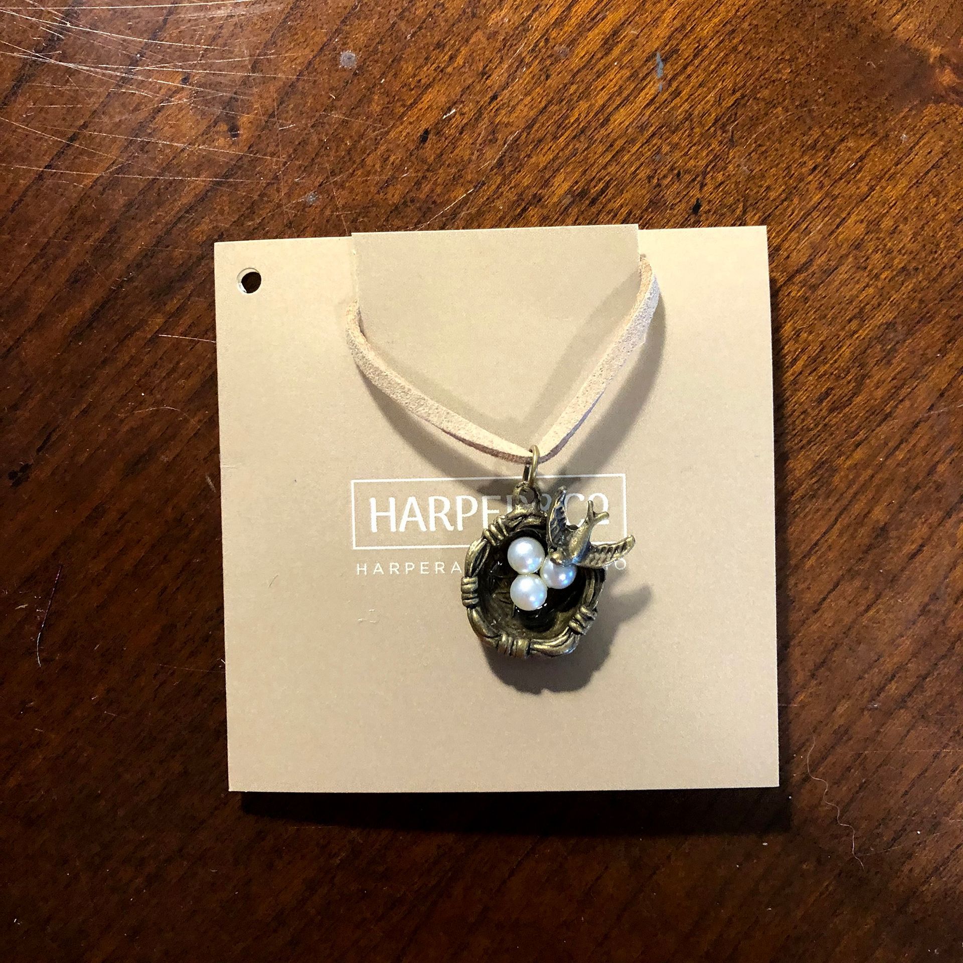 Necklace with bird's nest pendant on beige card, cream-colored ribbon, on a wooden table.