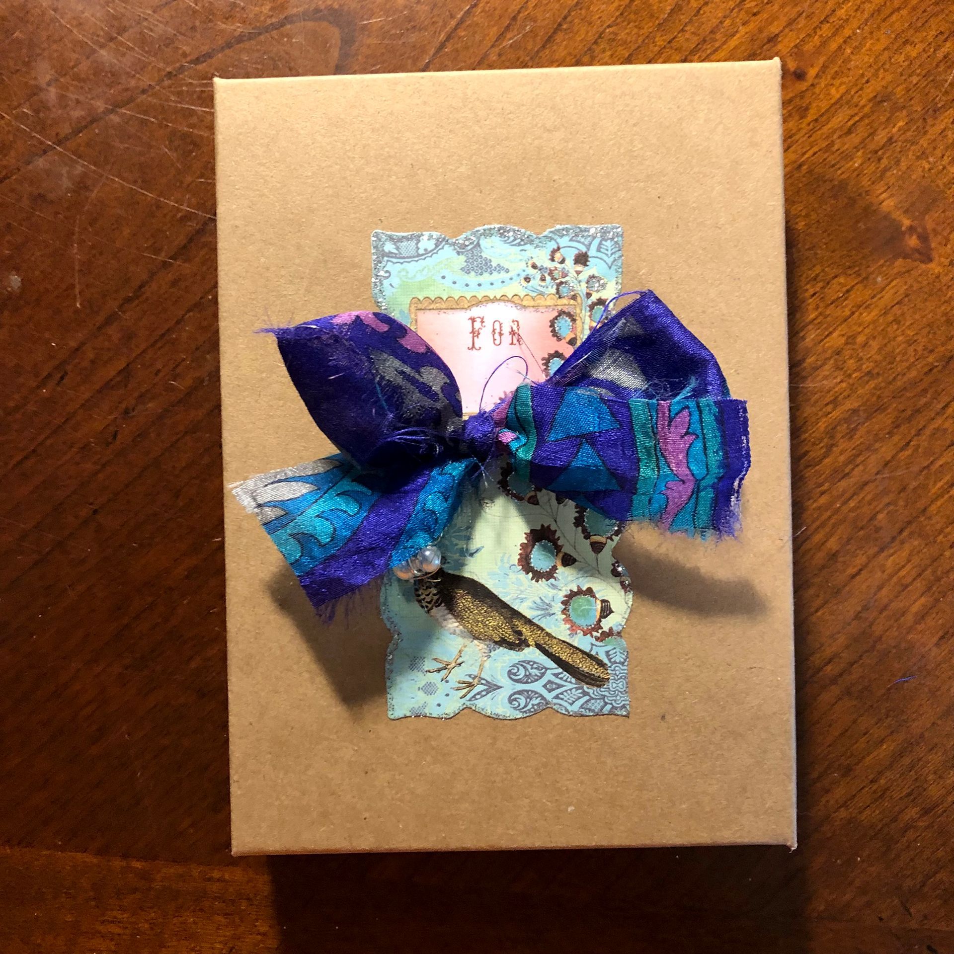 Brown box with decorative bow and layered paper embellishments.
