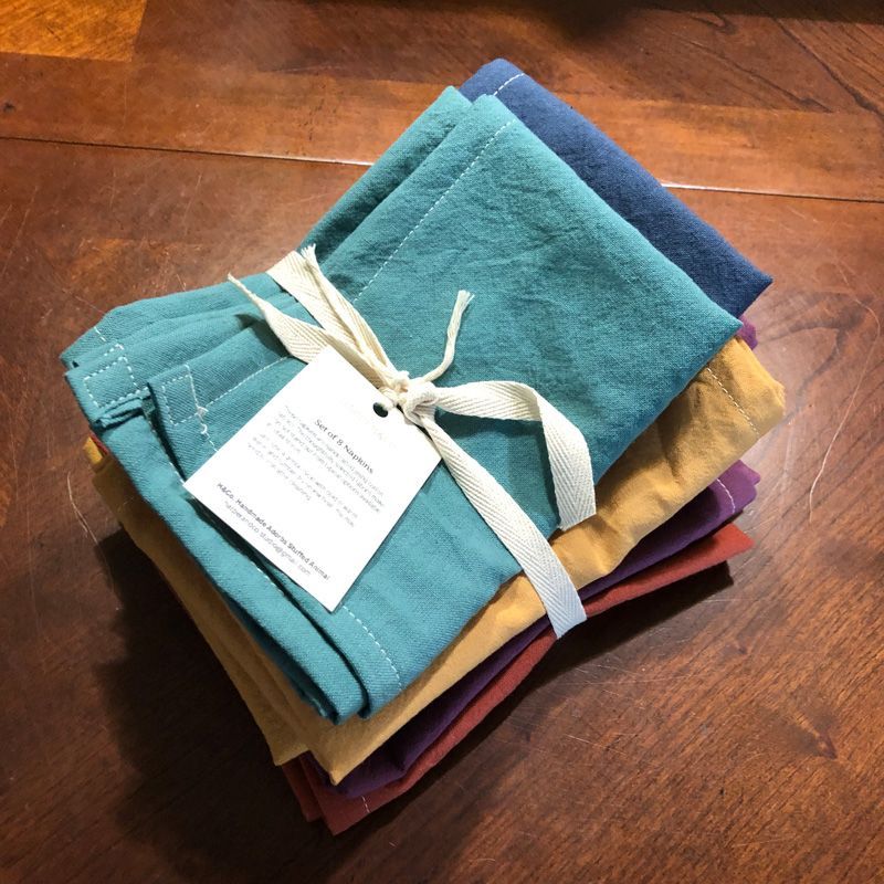 A stack of folded, multicolored fabric napkins tied with a white ribbon and a product tag on a wooden surface.
