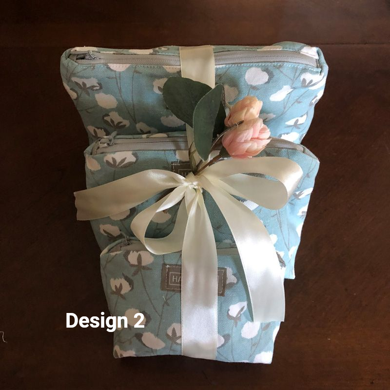 Two coral floral-print fabric pouches stacked together, accented with a large silk poppy, green leaf, and a ribbon.