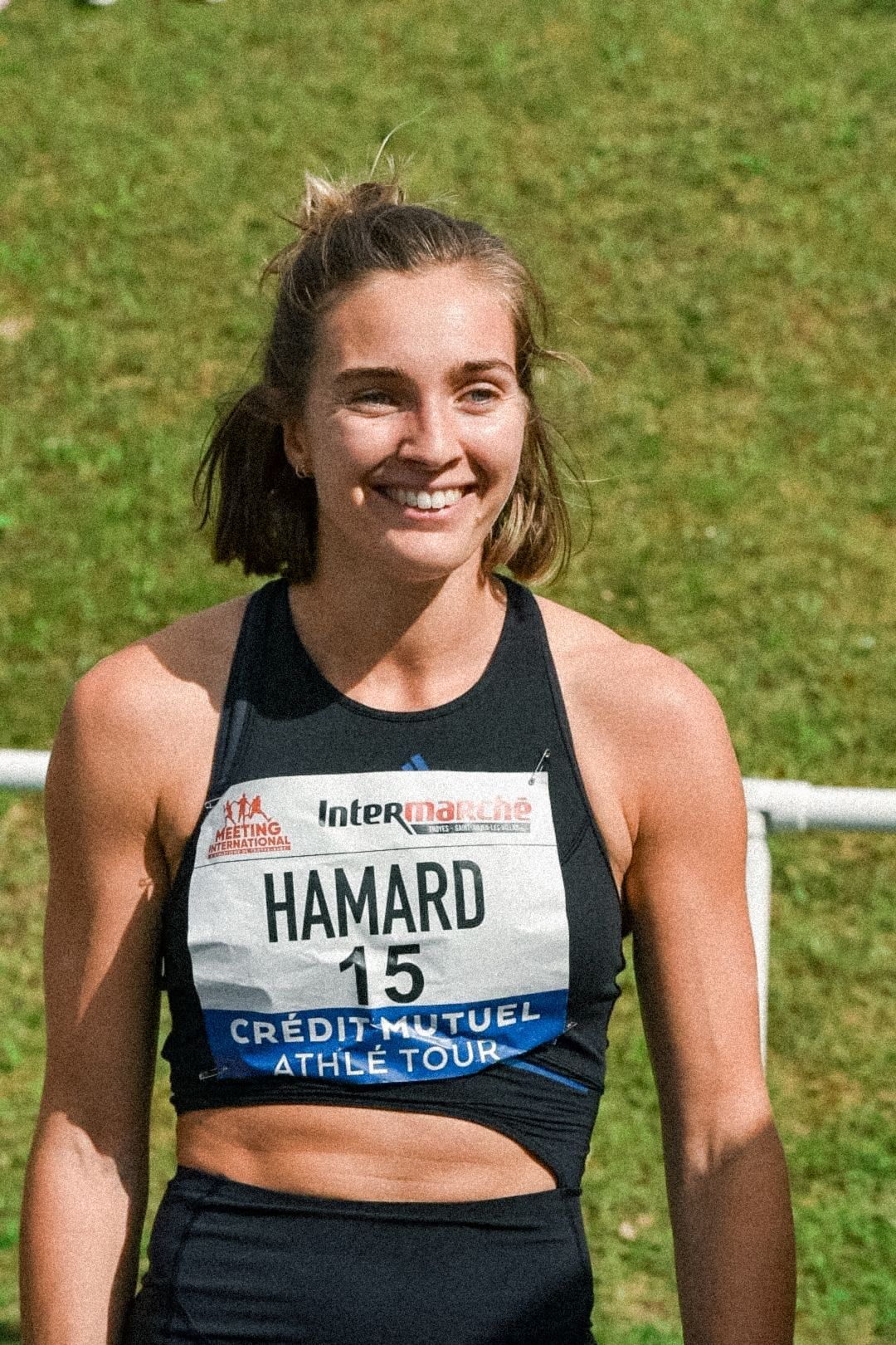 Une femme souriante portant un haut de sport et un dossard de course sur lequel est écrit « Hamard 15 ». Marion Hamard. 