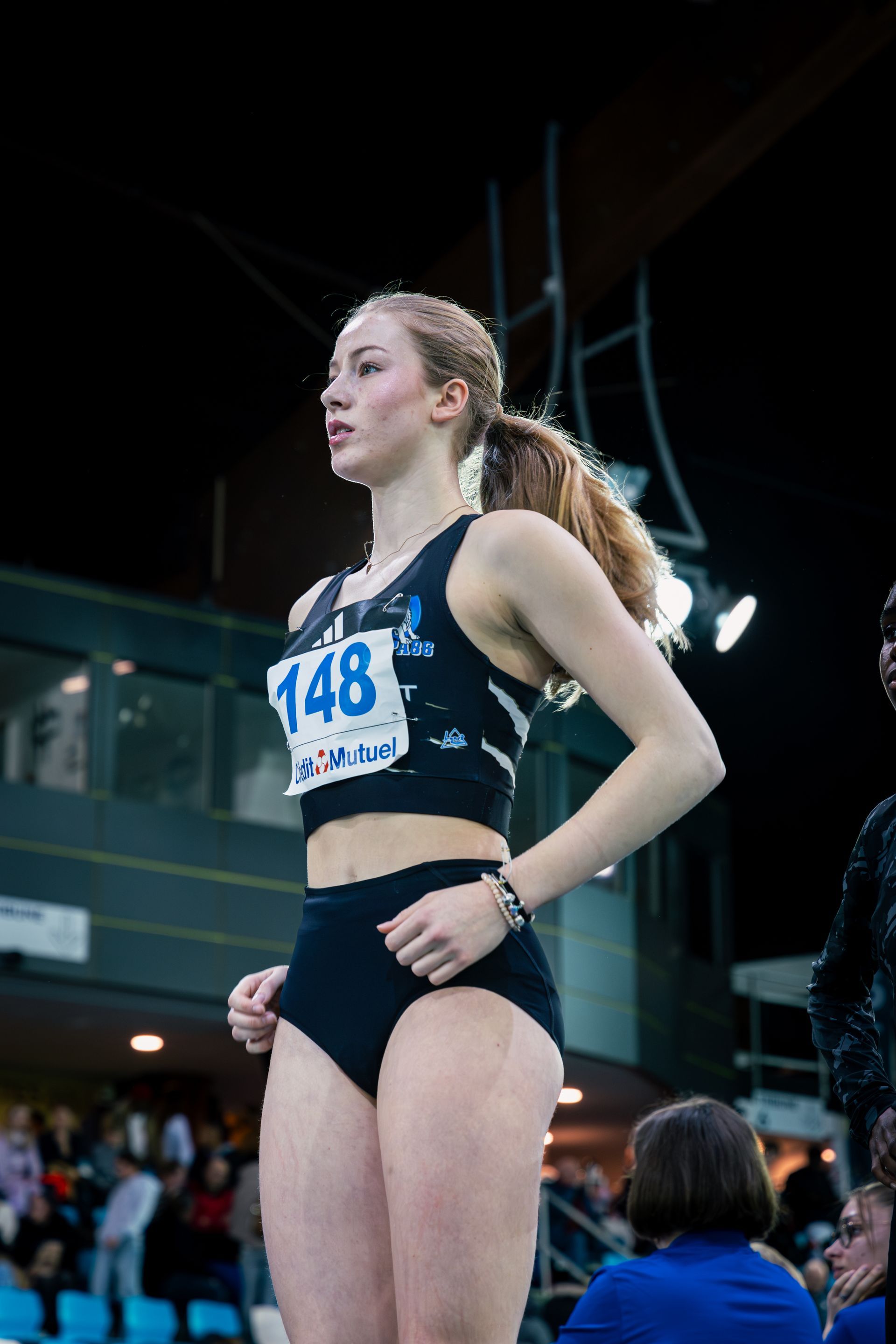 Athlète féminine en tenue de sport noire avec le numéro 148, piste intérieure, expression concentrée. Emma Gosset. 