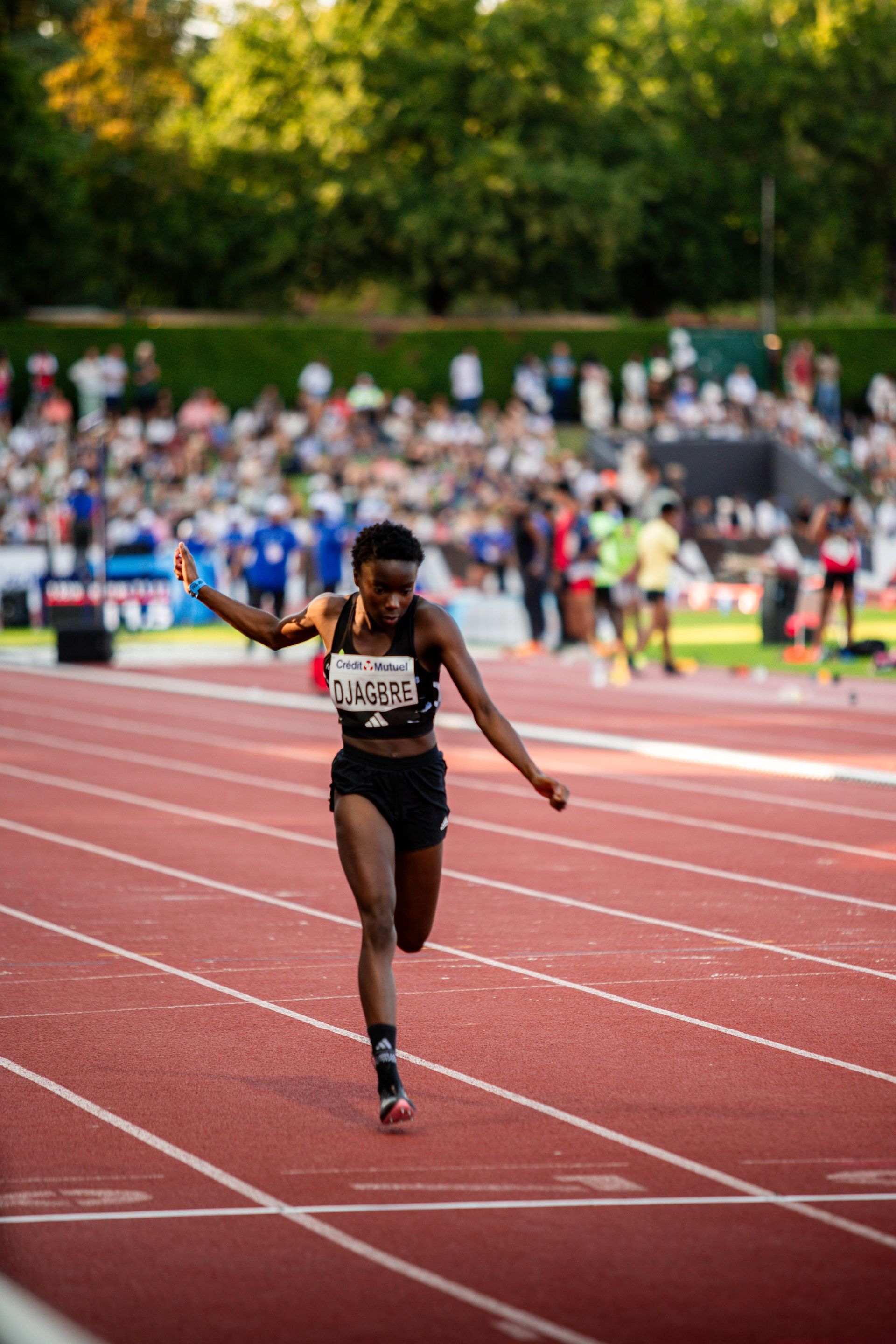 Sprinteuse  vêtue de la tenue noir et blanche EPA86, court sur une piste rouge à Talence. rose Djagbre. 