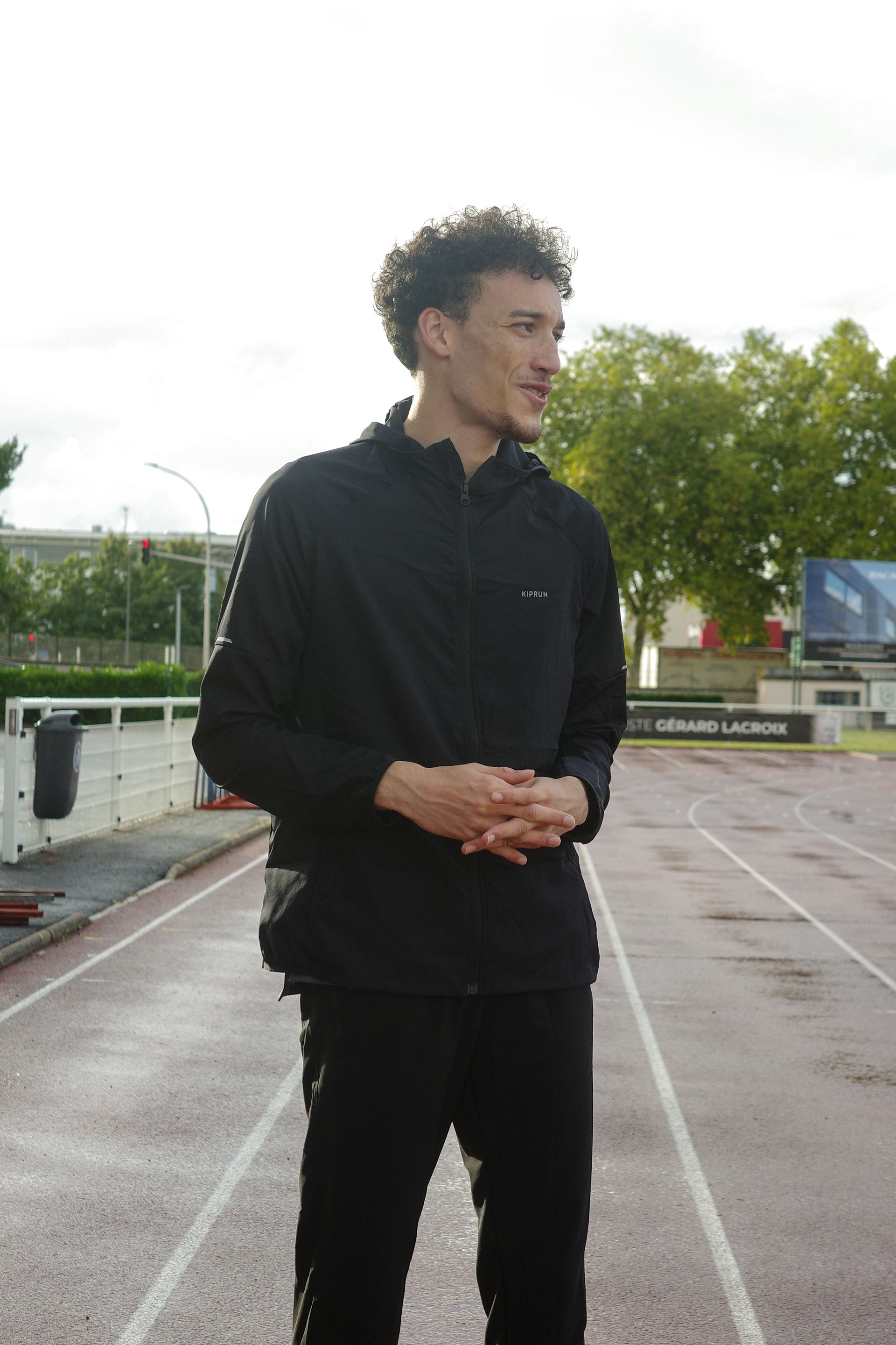 Un homme en tenue de sport noire se tient sur une piste de course, les mains jointes. Mathieu Lavie-Salomon.