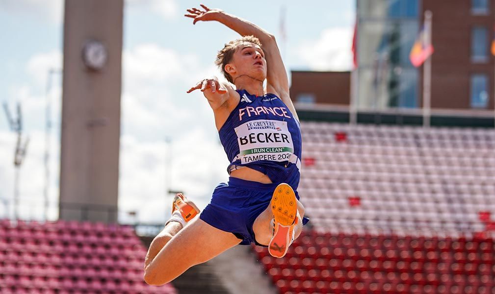 Un athlète français en uniforme bleu saute haut lors d'une compétition d'athlétisme.