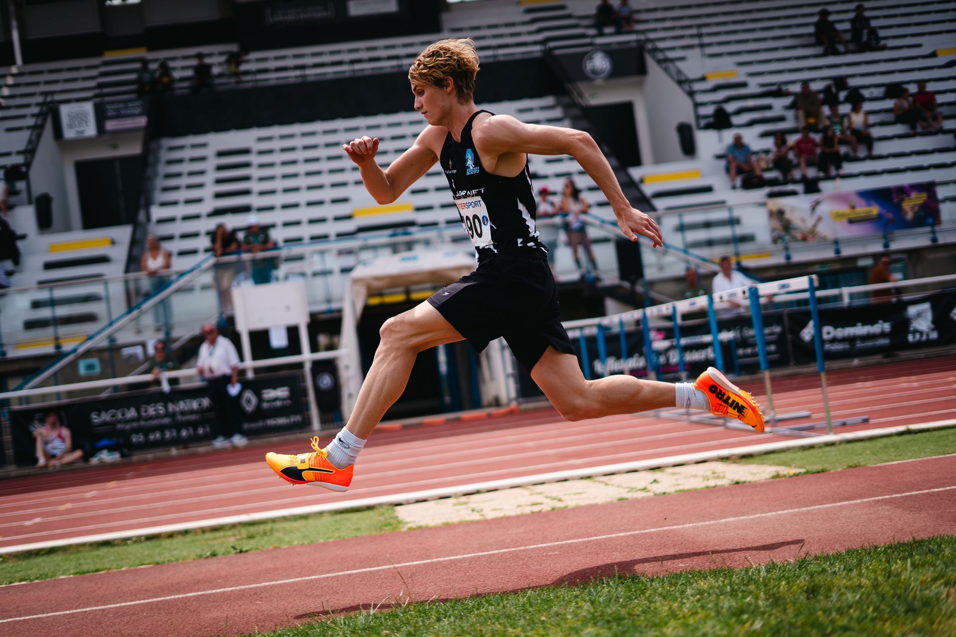 Sauteur en longueur masculin en uniforme EPA86,  s'élance  sur une piste, stade ensoleillé.