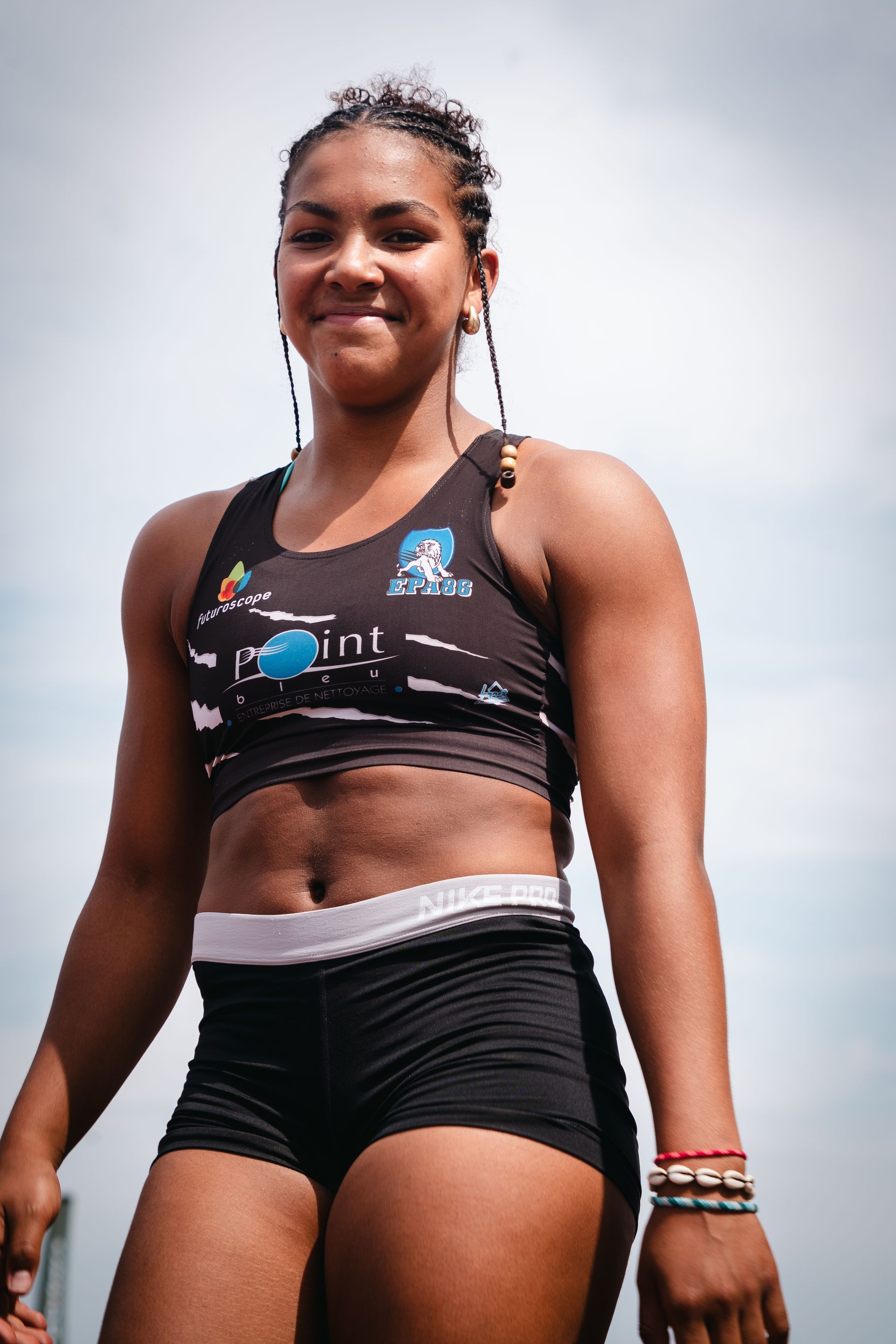 Femme noire souriante en tenue de sport, posant à l'extérieur. Violette Bray.