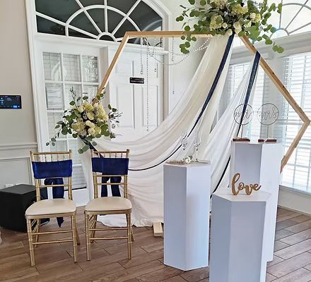 A room with a wooden arch , chairs , columns and flowers.