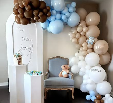 A teddy bear is sitting in a chair in front of a wall of balloons.