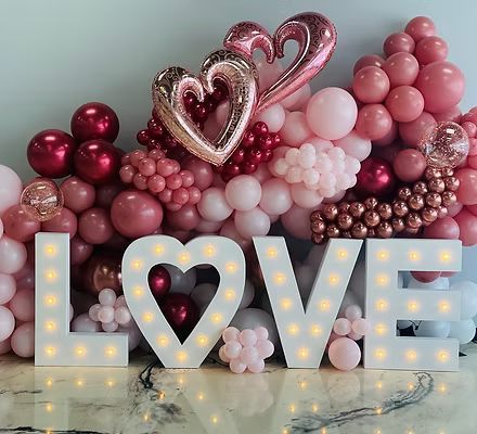 The word love is surrounded by pink and red balloons.