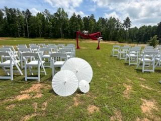 A row of white folding chairs and umbrellas in a grassy field.