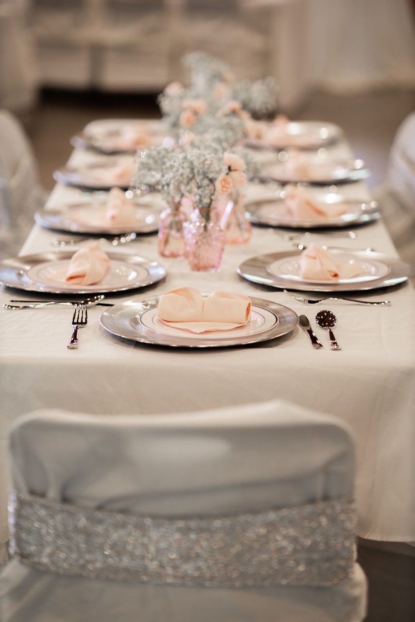 A long table with plates , silverware , and napkins on it.