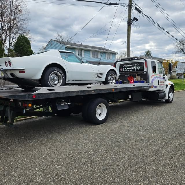 A white corvette is being towed by a tow truck