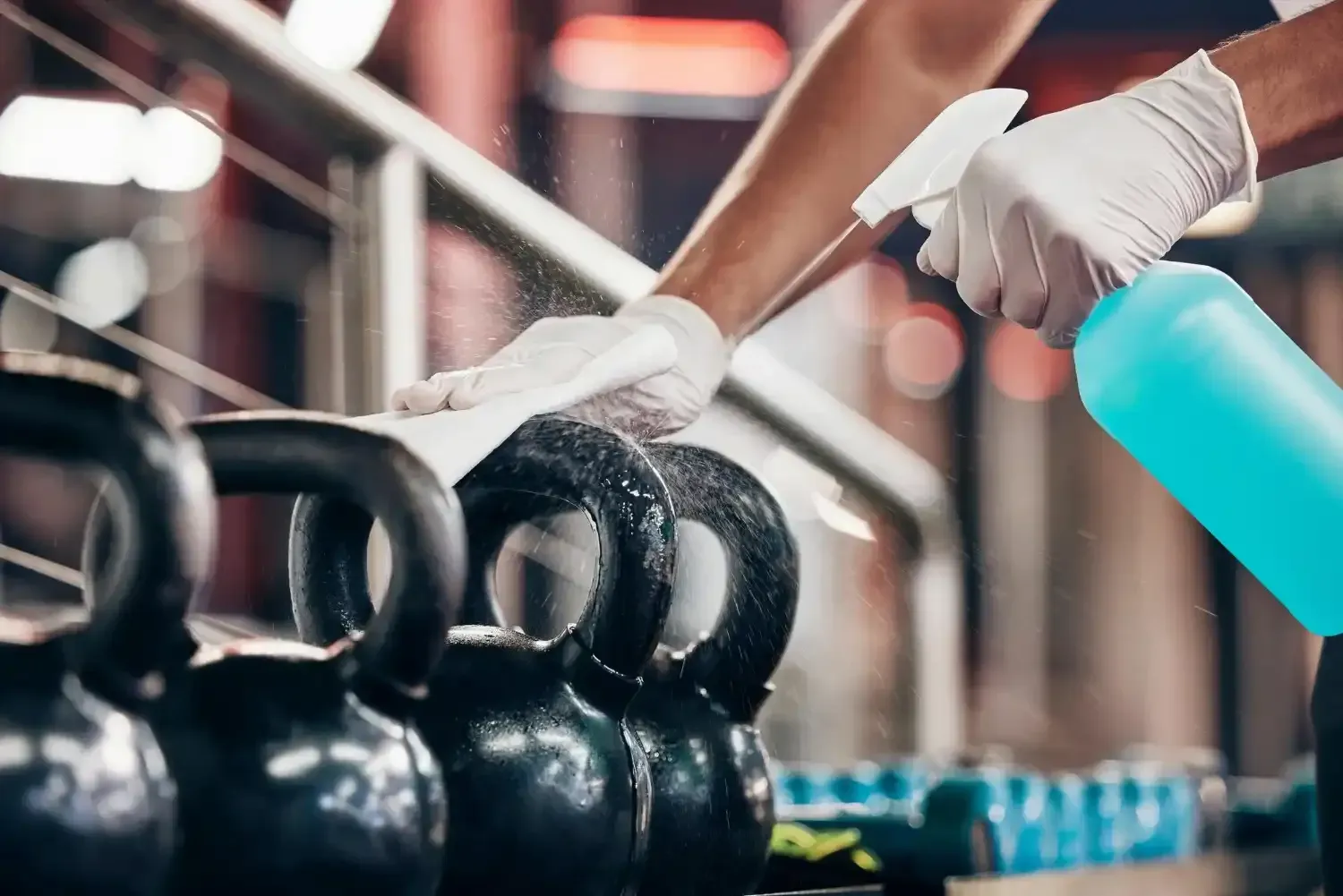 Person sanitizing kettlebells with spray and wipe at a gym.