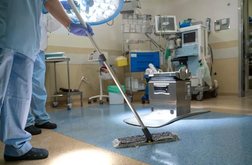 Person mopping the floor of an operating room; sterile environment with medical equipment.