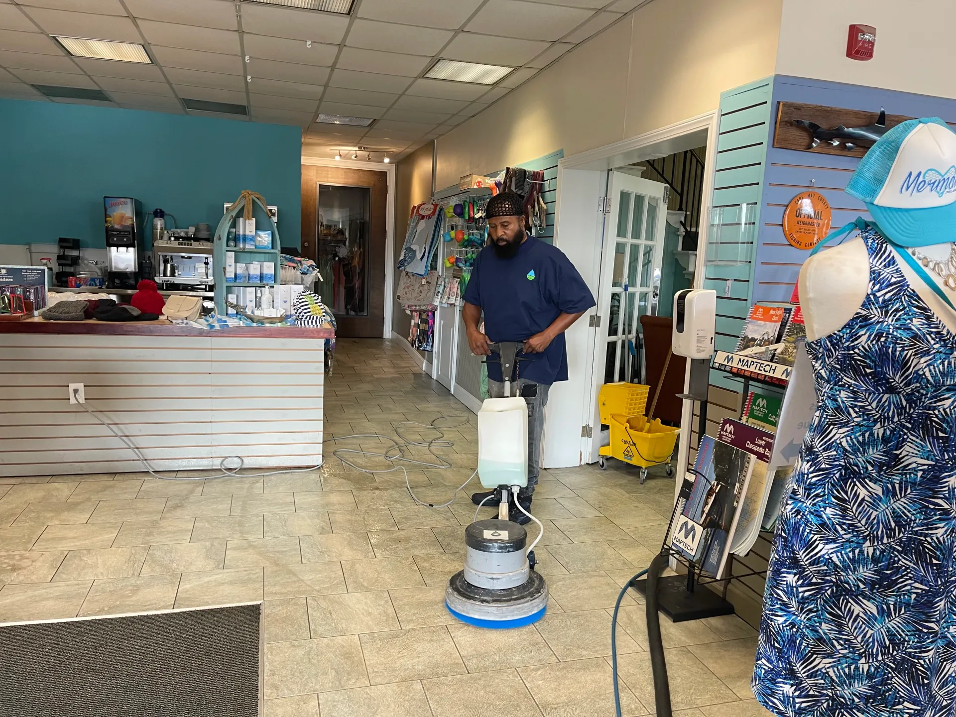 Man using floor buffer in a retail store, turquoise walls, display racks, doorway in background.