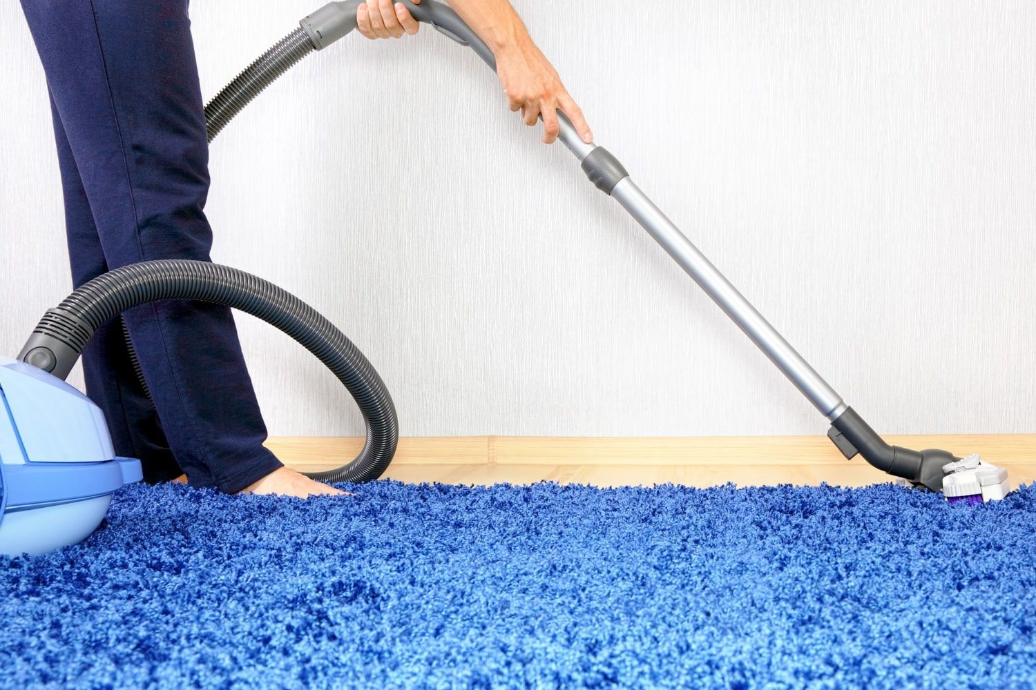 A person is using a vacuum cleaner to clean a blue carpet.