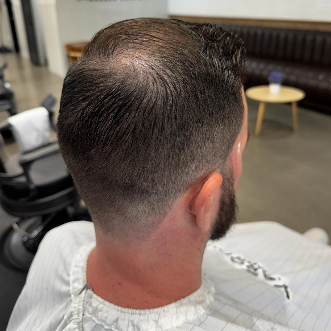Man with a fade haircut, seated in a barber's chair.  The back of his head shows thinning hair, a low fade on the sides and neck.