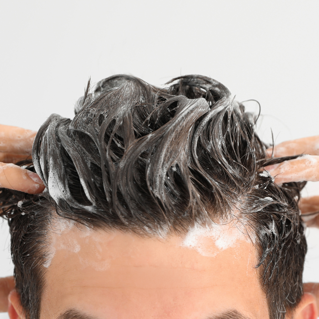 Man washing dark hair with shampoo, soapy foam, white background.