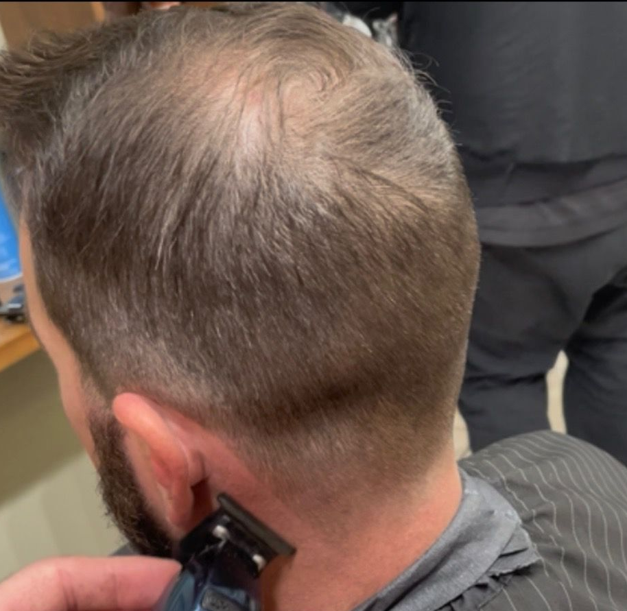 Man getting a haircut, showing the back of his head. Barber using clippers near the neck.