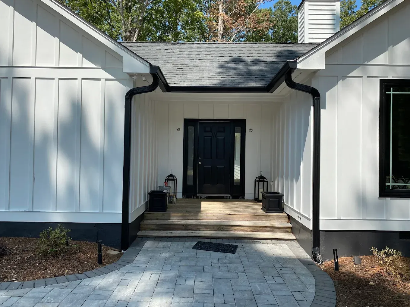 White house with black trim, front entrance with steps, and gray brick walkway.