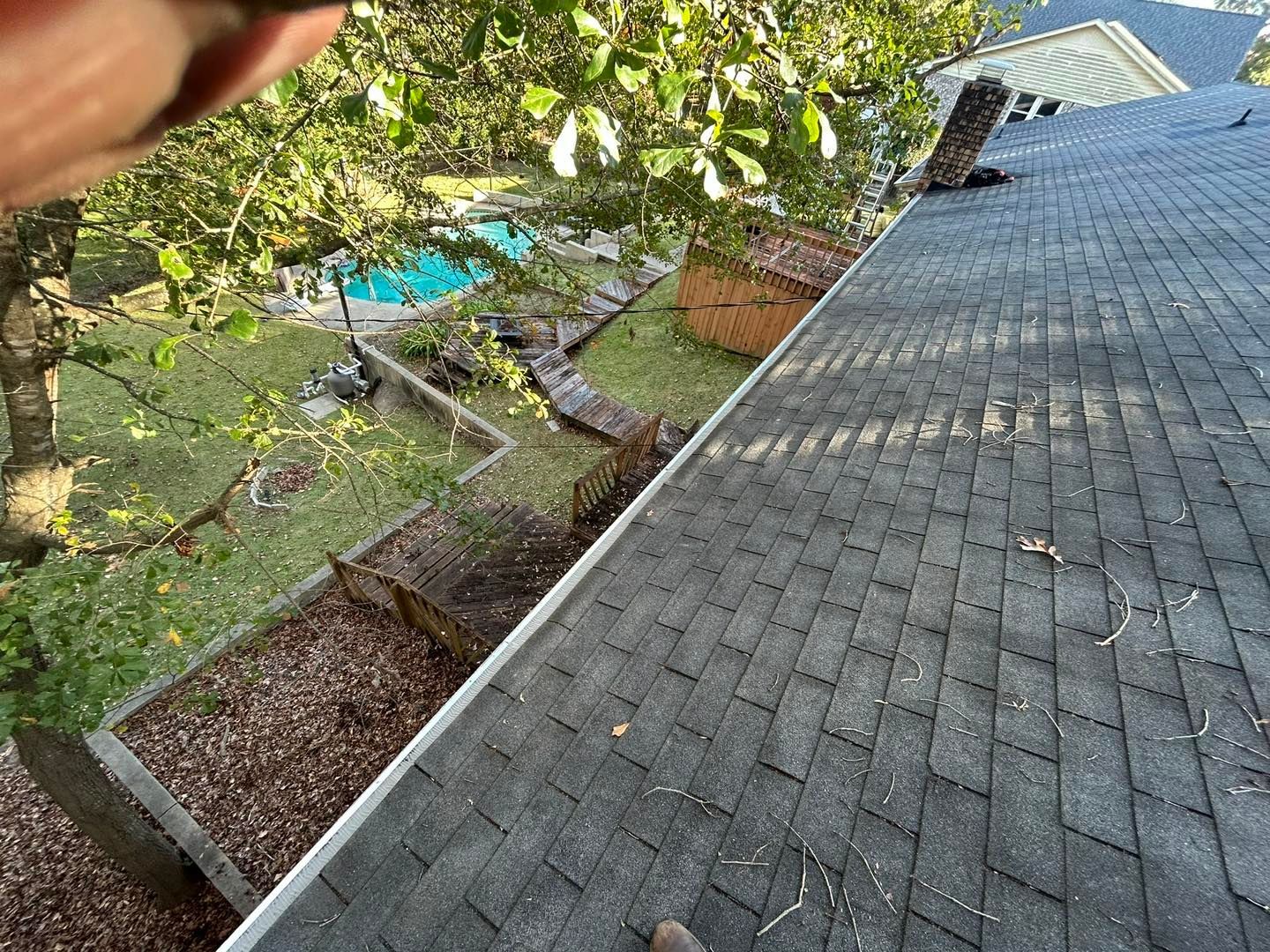 View from a roof of a backyard with pool, grass, and surrounding trees.