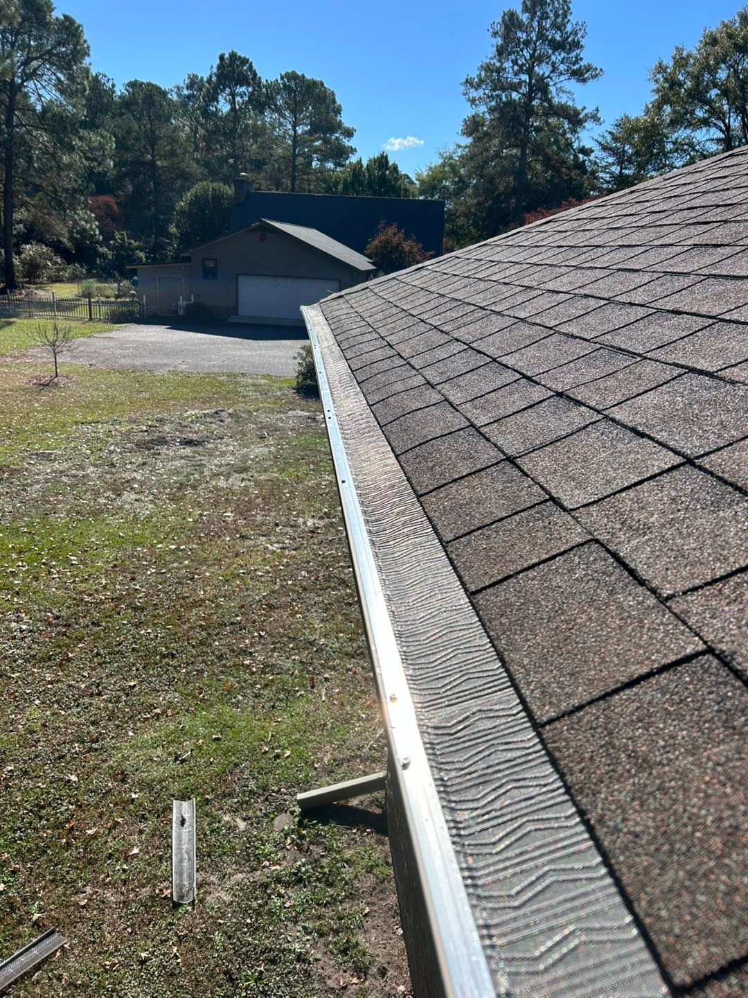 Roof of a house with gutter guard in front of a grassy yard, trees, and another building.