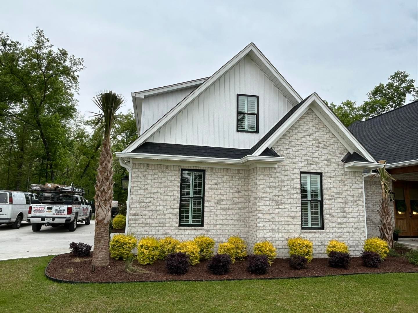 House with light brick facade and black trim, bushes in front.