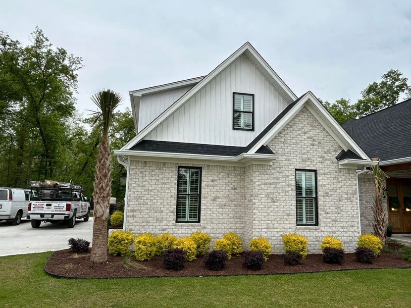 Modern house with white siding and brick, black-framed windows, and a landscaped yard.