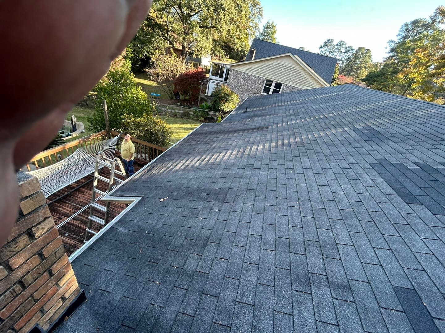 A dark shingle roof with a brick chimney and a partial view of a hand.