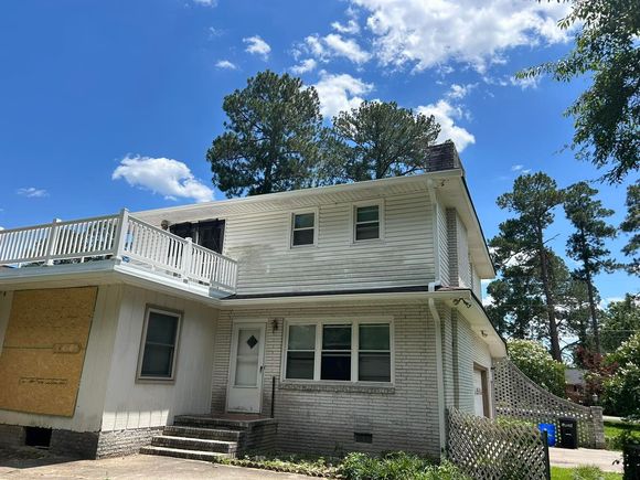 Two-story house with white siding and a balcony, under a partly cloudy blue sky.