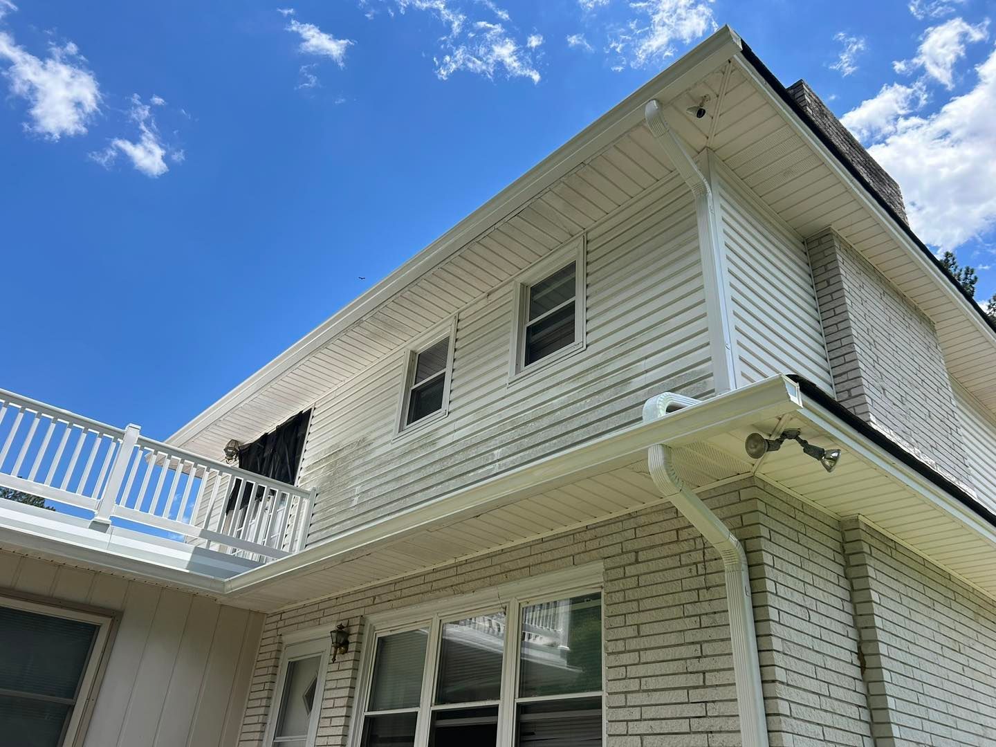 Exterior view of a two-story house with white siding and gutters. Blue sky with clouds in the background.