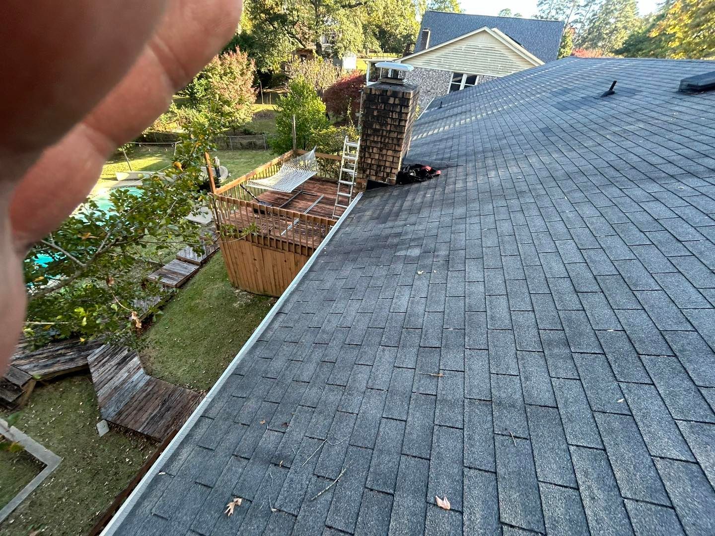 Roof with dark shingles and brick chimney, yard with pool in background.