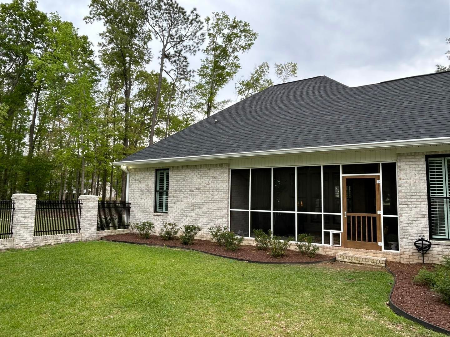 White brick house with screened porch, dark roof, and green lawn.