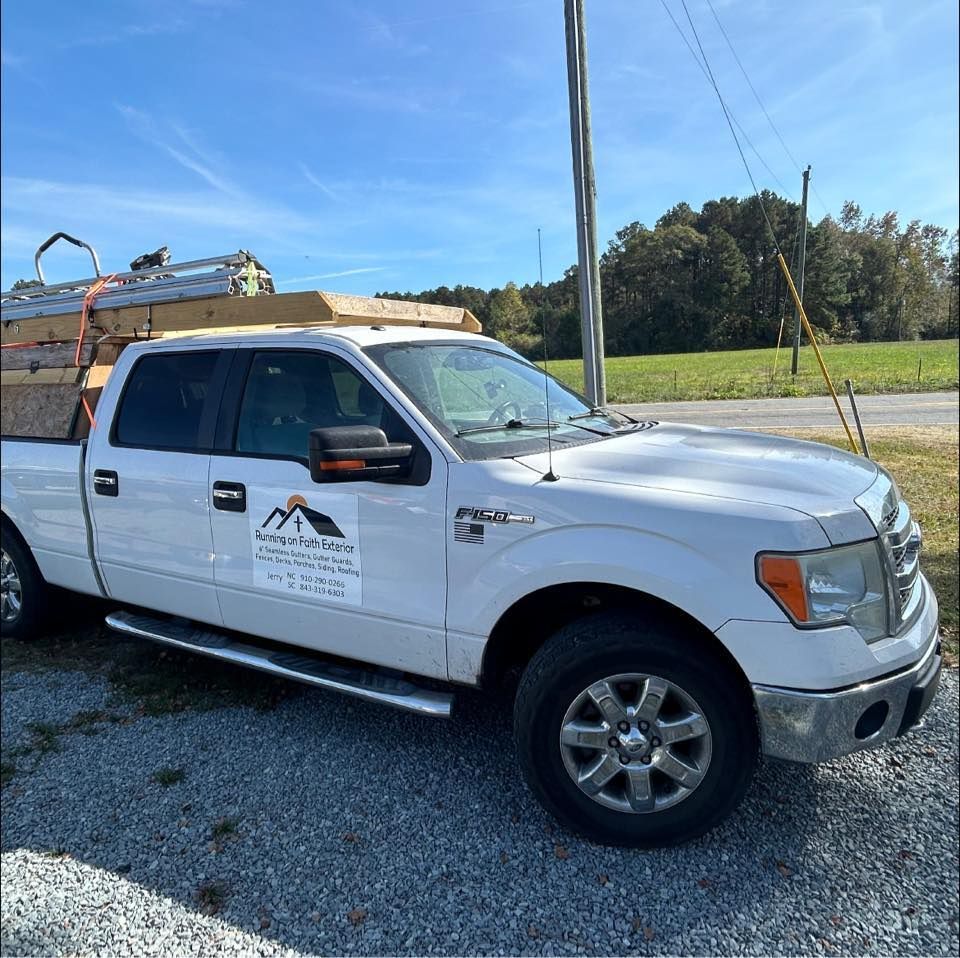 White pickup truck with roofing materials, parked on gravel with a sign that reads 