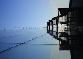 A tall building with glass walls reflects the blue sky and a row of dark window shades.